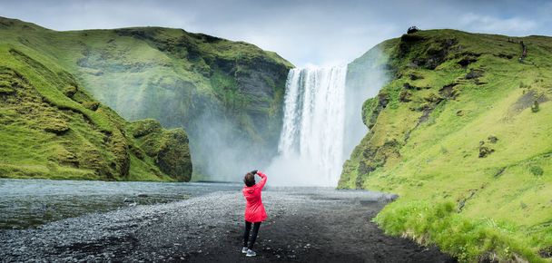 Молодая девушка, идущая рядом с водопадом Скогафосс летом, Исландия
 - Фото, изображение