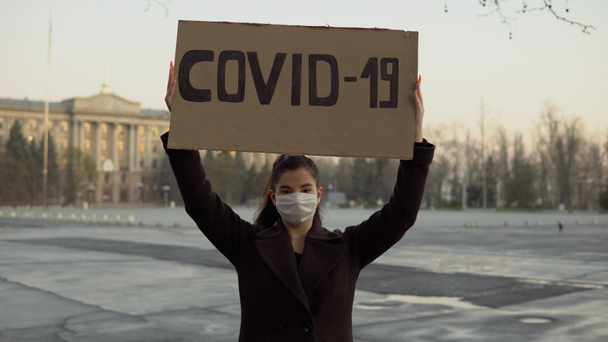Kızın elinde COVID-19 işareti var. Boş bir bölgede, karantina, koronavirüs, maske. - Fotoğraf, Görsel