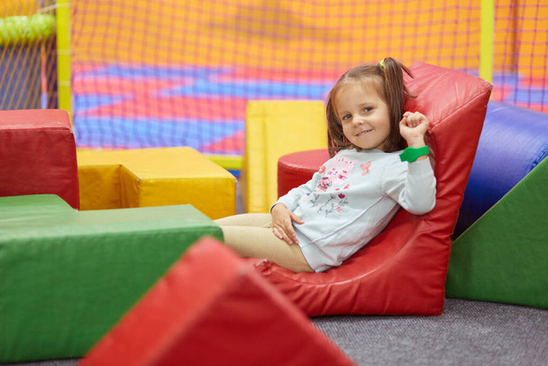 Indoor picture of relaxed joyful little child looking directly at camera, lying at playground, chilling out alone, being delighted with weekend time, having fun, wearing casual clothes. Child concept. - Photo, image