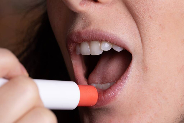 Closeup of woman putting pink lipstick on open mouth - Фото, зображення