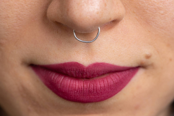 Makro einer durchbohrten weiblichen Nase und Lippen mit leuchtend rotem Lippenstift - Foto, Bild