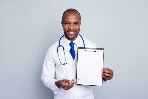 Photo of professional family doctor dark skin guy hold pen clipboard prescription insurance pharmacy showing place for signature wear lab coat tie stethoscope isolated grey color background - Foto, Imagem