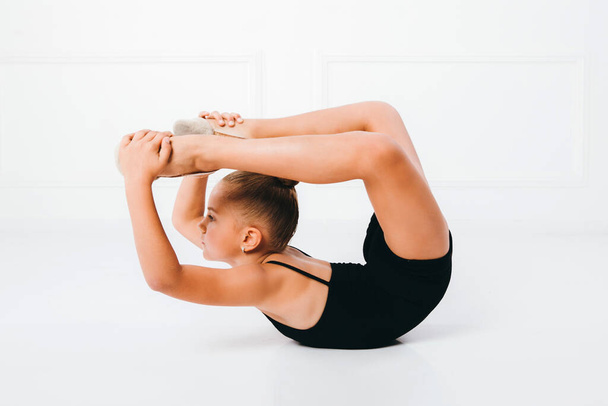 Chica joven haciendo ejercicio gimnástico sosteniendo sus pies con las manos sobre fondo blanco
 - Foto, Imagen