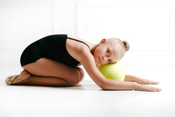Genç bayan atlet ritmik jimnastik, siyah bir takım elbise içinde yerde, kafası topun üstünde, kameraya bakıp gülümsüyor. - Fotoğraf, Görsel