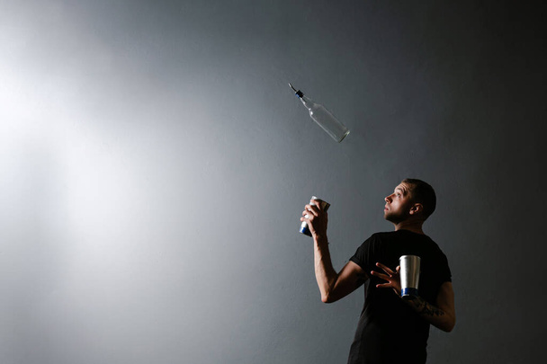 Professinal μπάρμαν άνθρωπος ζογκλέρ ένα μπουκάλι και σέικερ για κοκτέιλ στο κινητό μπαρ σε γκρι φόντο - Φωτογραφία, εικόνα