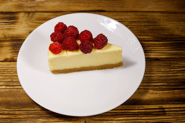 Pedaço de bolo de queijo de Nova Iorque saboroso com framboesas em uma chapa branca na mesa de madeira - Foto, Imagem