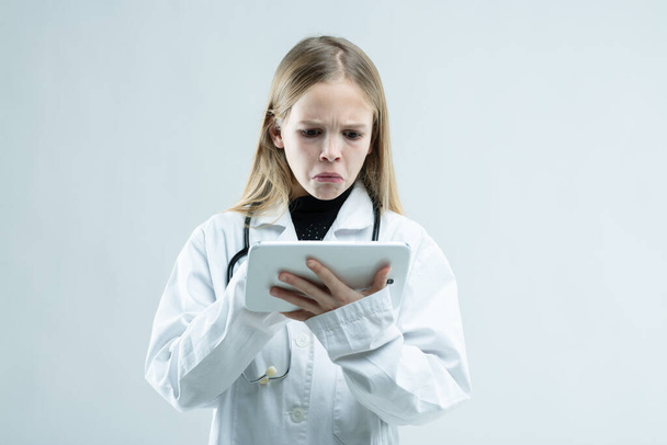 Jeune fille en blouse blanche plissant sur un presse-papiers avec une expression morose comme elle prétend être un médecin ou une infirmière isolé sur blanc
 - Photo, image