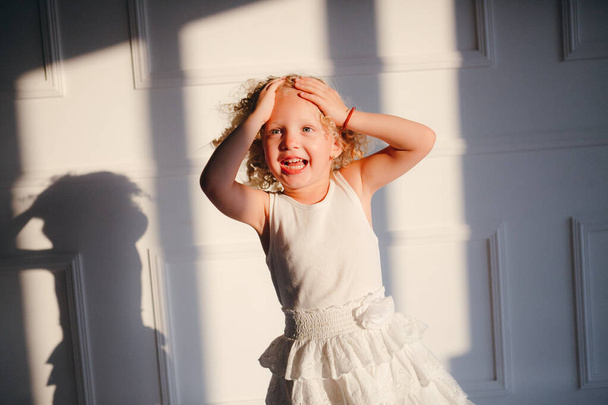 Ein blondes, lockiges Mädchen im weißen Kleid tanzt, lacht, springt - Foto, Bild