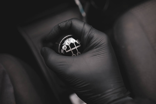 Details with the hand of a driver, in a latex glove, on an old and broken gear shift knob of a manual gearbox car during the Covid-19 pandemic. - Fotó, kép