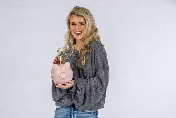 Uma linda modelo loira segurando um banco porquinho e economizando dinheiro
 - Foto, Imagem