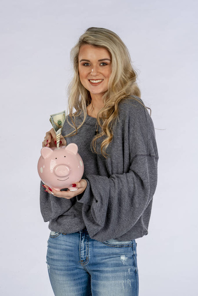 Een prachtig blond model met een spaarvarken bank en geld besparen - Foto, afbeelding