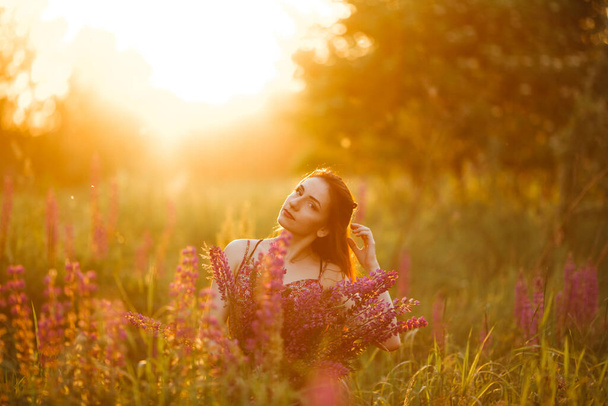 girl holding flowers. Brunette in field. sunset. - Fotó, kép