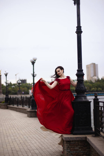 Young brunette woman in a red dress with a train. Evolving in the wind - Fotografie, Obrázek