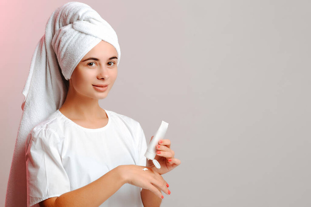 Young woman in a head towel and white t-shirt applying cream on hand from the tube. Making the skin clean, smooth and moisturized. - Foto, imagen