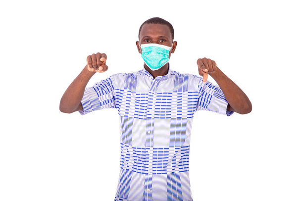 un giovane uomo con una camicia in piedi su uno sfondo bianco che indossa una maschera medica e punta il dito contro qualcuno
. - Foto, immagini