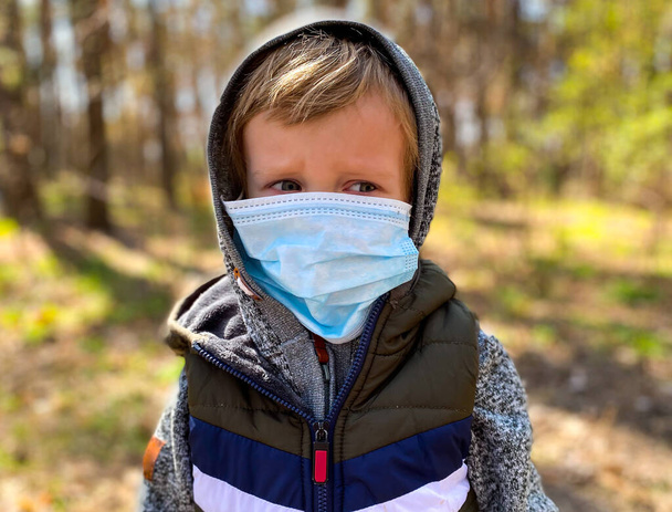  Κοντινό πλάνο ενός μικρού ανοιχτόχρωμου παιδιού με προστατευτική ιατρική μάσκα. - Φωτογραφία, εικόνα