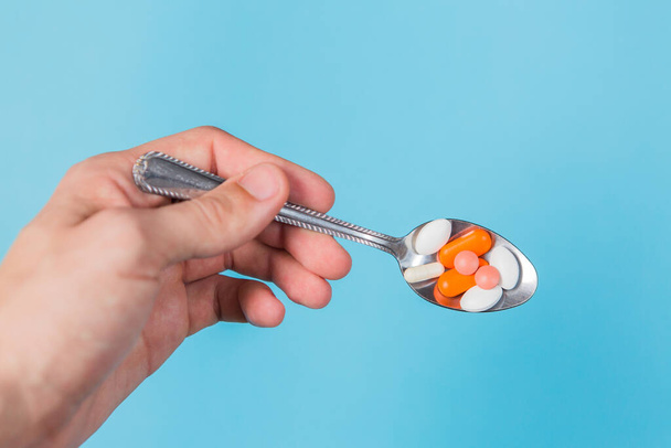 Hand holding metal spoon with different pills on a blue background. health and medicine - Foto, afbeelding
