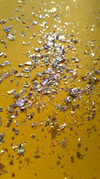 Foil pieces on yellow background with multi colored shine. Abstract fashion stock macro photo. - Photo, Image