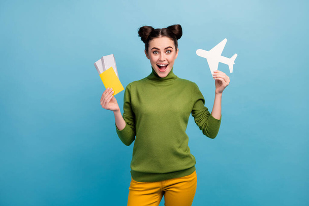 Photo of funny excited lady hold paper air plane passport tickets addicted traveler buy cheap tour abroad wear green turtleneck yellow trousers isolated blue color background - Fotografie, Obrázek