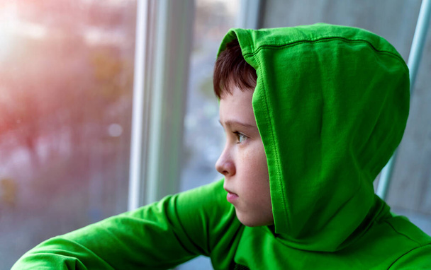 Young boy looks out of a window during the coronavirus COVID-19 quarantine period. Disease outbreak forces people stay at home. Infection prevention and isolation concept. - Foto, Imagen