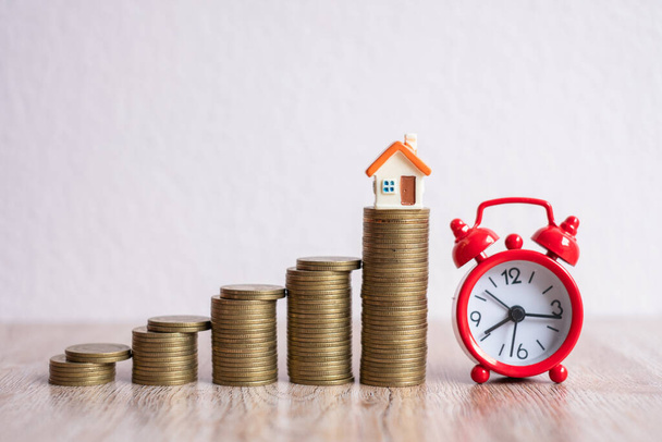 Red alarm clock Placed near the pile of coins with the house on top.The idea of making good use of time And choosing to invest in a residential business during that time may be at risk. - Photo, Image