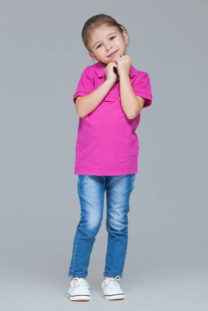 Full length portrait of funny active little girl wearing casual clothes: jeans and pink t-shirt isolated on grey studio background - Foto, immagini
