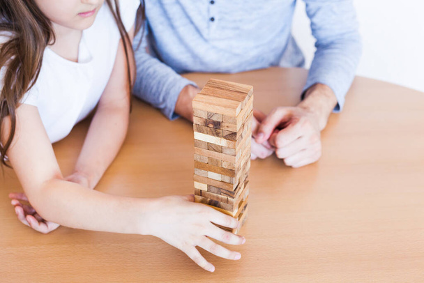 Girl and dad play a game at home, cost a tower of blocks, cubes, jenga, puzzle for brain development, mental intelligence, child development, school, home, quarantine, vacation, time with family - Foto, Imagem