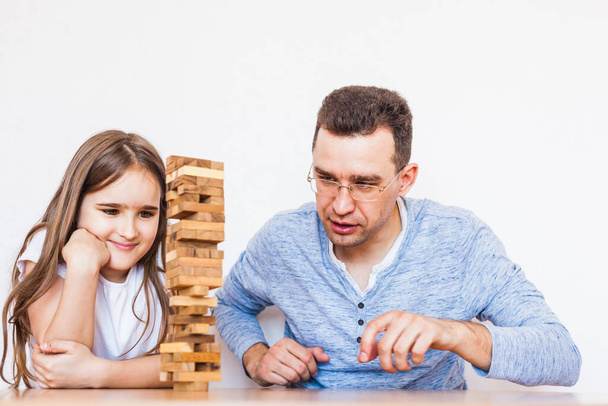 Girl and dad play a game at home, cost a tower of blocks, cubes, jenga, puzzle for brain development, mental intelligence, child development, school, home, quarantine, vacation, time with family - Foto, afbeelding