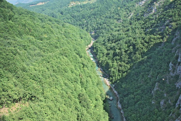 Most na rzece Tara w Czarnogórze i most łączący dwa brzegi kanionu. Kamienne łóżko czystej rzeki przepływające przez dolinę wzdłuż drogi na zboczu góry. - Zdjęcie, obraz