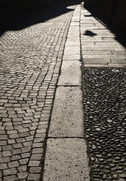 Vicenza 'nın merkezindeki bir caddenin kaldırımının detayları. Bazaltik taşta kare elementler, dikdörtgen levhalarda kaldırım ve kaldırımlar. Öğleden sonra ışığı, caddenin karşısına uzanan gölgeler.. - Fotoğraf, Görsel