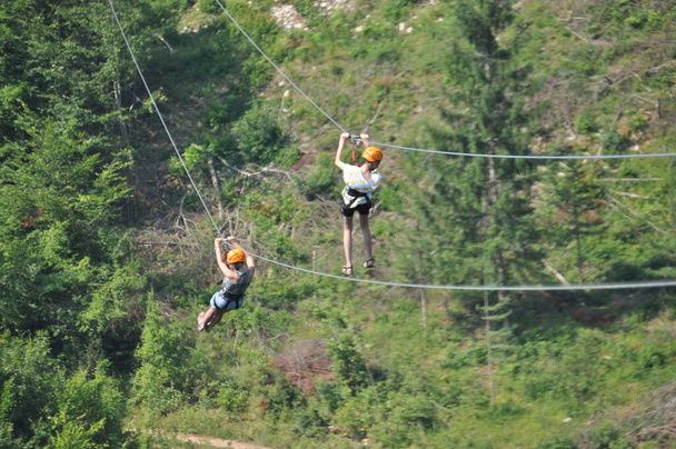 Mutter und Tochter auf einer Seilrutsche über die Tara-Schlucht, einem Fluss in Montenegro mit der tiefsten Schlucht Europas. Mädchen im Geschirr mit Helm auf dem Kopf. - Foto, Bild