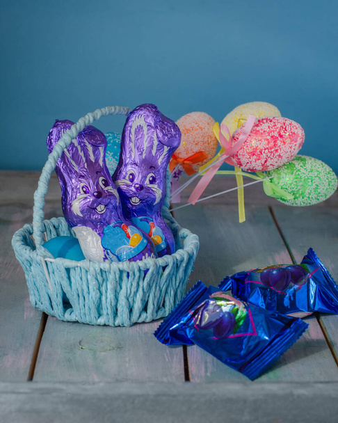 Liebres de chocolate morado en una canasta de mimbre y bolas de colores. Tarjeta de felicitación de Pascua
. - Foto, Imagen