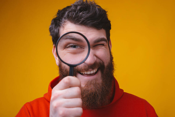 close-up portret van een man met baard kijken door een vergrootglas. - Foto, afbeelding