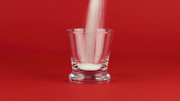 Ρίξτε ζάχαρη σε ένα γυάλινο πλάνο με ένα παχύ πυθμένα σε ένα κόκκινο φόντο αντίθεση - Πλάνα, βίντεο