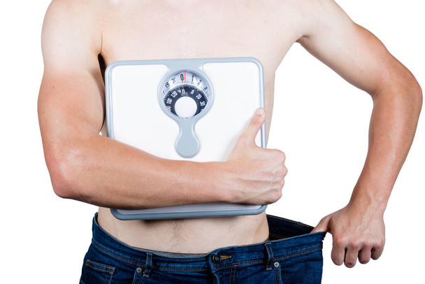 Концепція втрати ваги, що показує м'язистого молодого дорослого чоловіка, який тримає мішкуватий одяг, що тримає шкала ванної кімнати
 - Фото, зображення