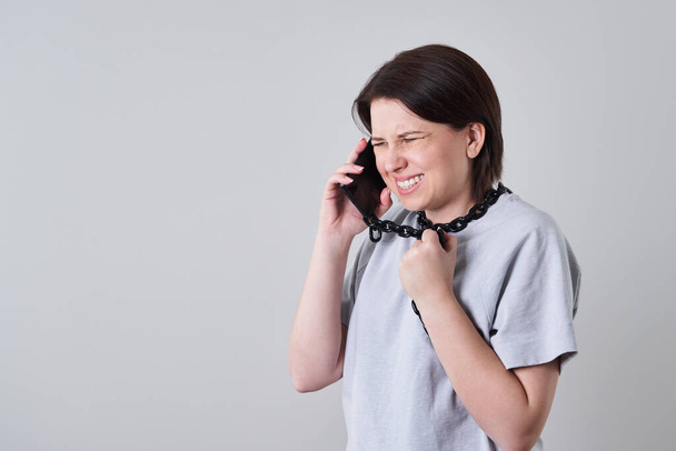Γυναίκα μιλάει σε αλυσοδεμένο κινητό τηλέφωνο πάνω από γκρι φόντο, έννοια του εθισμού - Φωτογραφία, εικόνα