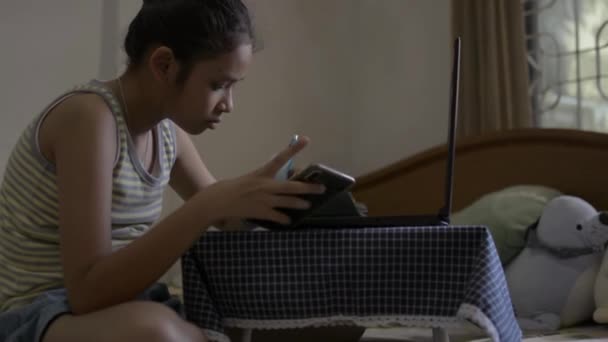 Asian cute girl in singlet shirt watching lesson online during doing homework on the bed. Female teenager studying from home with video call during COVID-19 outbreak situation. - Felvétel, videó