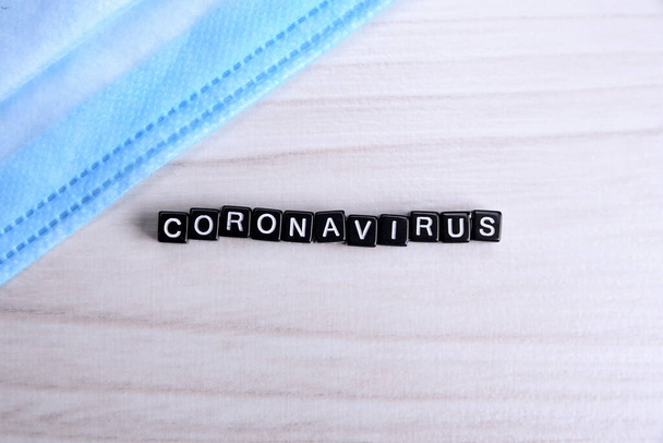 das Wort Coronavirus mit silbernen Buchstaben auf zerknüllte blaue Plastikfolie gelegt - zentrierte flache Lagekomposition mit dramatischem Licht - Foto, Bild