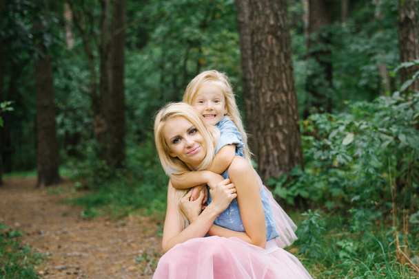 Äiti ja viisivuotias tytär identtisissä vaaleanpunaisissa tyllihameissa ja sinisissä farkkupaidoissa kävelevät puistossa tai metsässä. Tytär halaa äitiään. Äitienpäivä - Valokuva, kuva