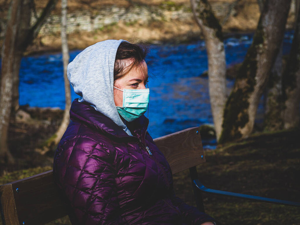 Donna triste seduto da solo sulla panchina nel parco indossando maschera per evitare infettive. Il virus Corona, o Covid 19, si sta diffondendo in tutto il mondo.  - Foto, immagini