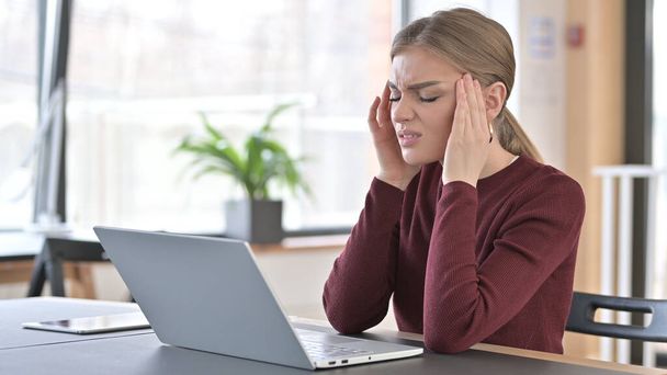 Mujer joven con dolor de cabeza utilizando el ordenador portátil en la oficina
 - Foto, imagen