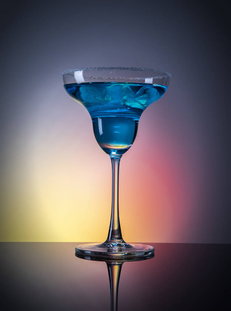 Стекло с голубым напитком и льдом на фоне цветового градиента
 - Фото, изображение