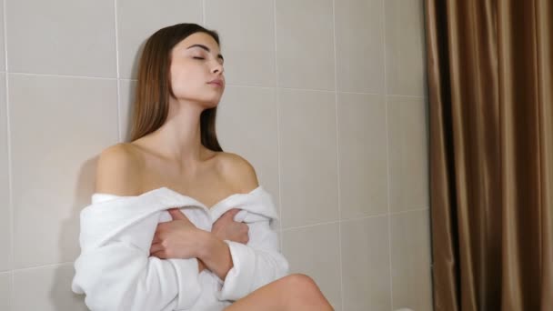 Portrait of young happy brunette woman in bathrobe relaxing and enjoying herself. Sweet female person with natural smile liking her face and hair, selfconfident and satisfied with her appearance. Shot - Footage, Video