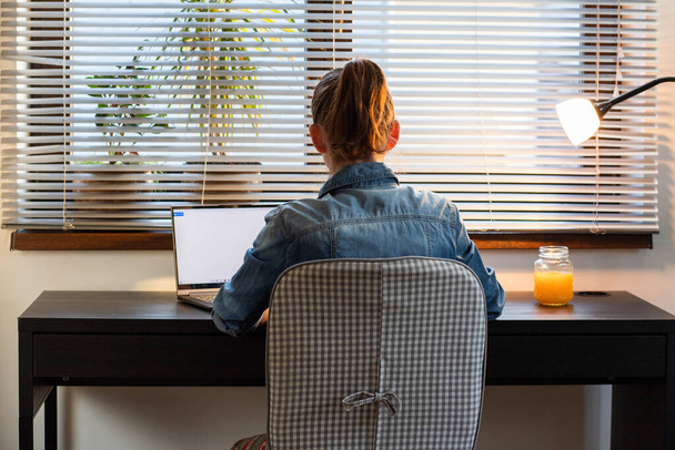 自宅のオフィスの女性はコピースペースのための夕暮れの白い画面でコンピュータ上で作業 - 写真・画像