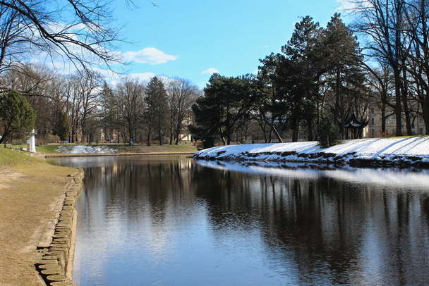 Centro tranquilo de la ciudad de Riga. Parque público y vista al canal de la ciudad con la última nieve en esta temporada
. - Foto, Imagen