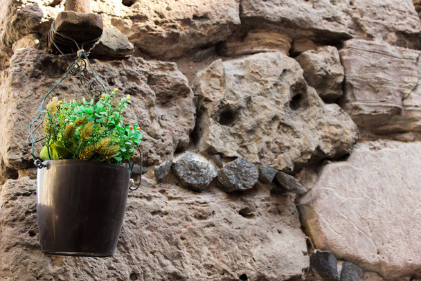 Vieille paroi faite de rochers. Texture d'un vieux rocher collé avec un ciment. Petit pot de fleur suspendu au mur
.  - Photo, image