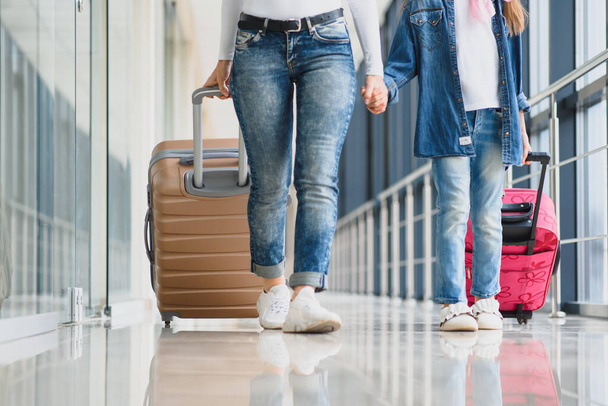Happy young mother and her daughter walking in the airport terminal while carrying a suitcase. High season and vacation concept. Relax and lifestyles - 写真・画像