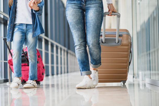 Happy young mother and her daughter walking in the airport terminal while carrying a suitcase. High season and vacation concept. Relax and lifestyles - Foto, imagen