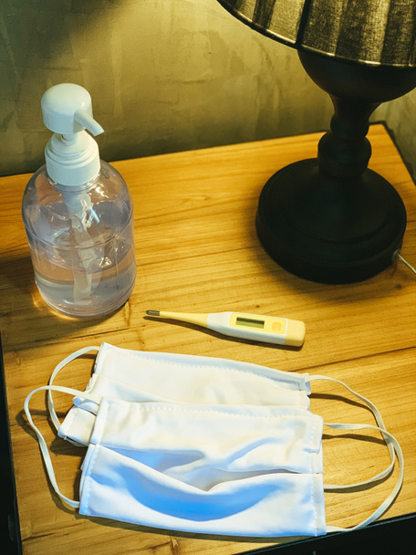 Coronavirus prevenção máscaras cirúrgicas médicas, gel higienizador de mãos e termômetro na mesa de madeira. Conceito de higiene pessoal
 - Foto, Imagem