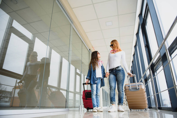 Beautiful mother and her stylish cute daughter walk together and pull a pink suitcase at airport. High season and vacation concept. Relax and lifestyles - Fotó, kép